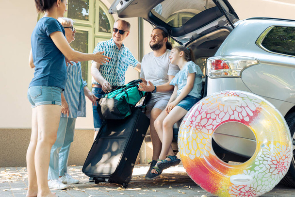 European family loading bags in trunk vehicle, preparing to leave on seaside vacation journey. Little child with parents and grandparents travelling with automobile to go on summer holiday. - Foto, imagen