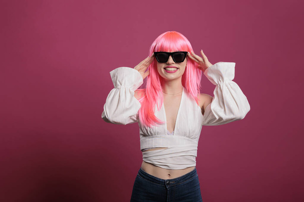 Glamour πρόσωπο με κομψό στυλ μόδας φορώντας μοντέρνα γυαλιά ηλίου, έχοντας αυτοπεποίθηση και σέξι στάση με ροζ μαλλιά. Αίσθηση ξέγνοιαστη και αισθησιακή με μοντέρνα κομψά γυαλιά στο studio. - Φωτογραφία, εικόνα