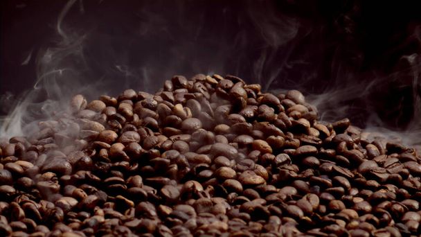 Steam rising over hot coffee beans heap close up. Roasting process caffeine seeds in slow motion. Fragrant coffee grains on pile with great aroma. Perfect ingredient for preparing energetic beverage. - Valokuva, kuva