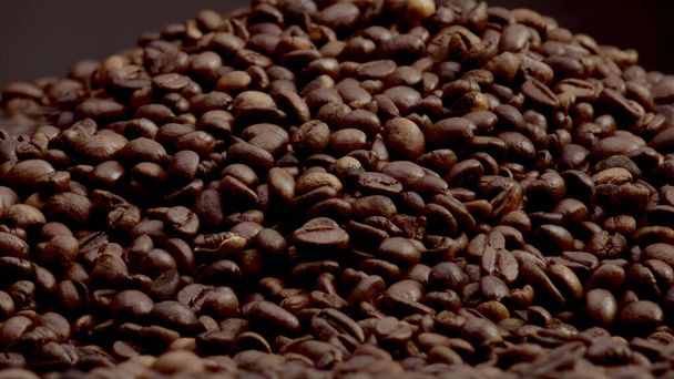 テクスチャコーヒー粒の背景を閉じます。超スローモーションでローストブラウンの種から来る軽い芳香の蒸気。濃い背景に新鮮なオーガニックコーヒーヒープ。カフェイン飲料の原料. - 写真・画像