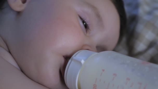 Portrait of a little child falling asleep with a bottle in his mouth. The child eats in his sleep. The baby drinks milk from a bottle and sleeps. High quality 4k footage - Imágenes, Vídeo