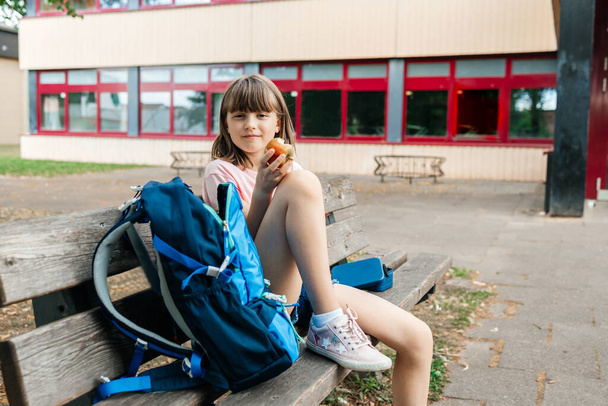 A teenage schoolgirl sits on a bench next to the school and eats lunch. Healthy eating for children while studying. - Valokuva, kuva