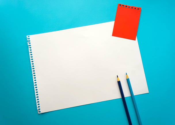 Blank sheet of paper space for design and lettering on a beautiful blue background, blue pencils. A sheet of perforated paper torn from a notepad rests obliquely on the surface. Square sheet copyspace - Foto, immagini