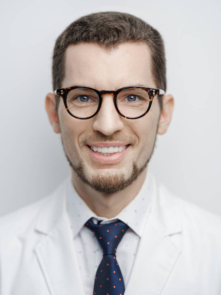 Portrait of happy stylish young bearded male doctor with pretty smile. Model wearing eyeglasses, coat and tie isolated on white background - Foto, afbeelding