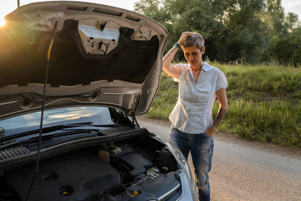 one woman mature caucasian female standing on the road by the broken vehicle car automobile failed engine open hood making waiting for help carefree copy space - Fotoğraf, Görsel