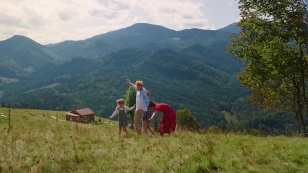 Happy family having fun playing on green hill sunny day. Joyful people running with outstretched hands outdoors at summer vacation. Cheerful parents with children enjoying time together in mountains. - Záběry, video