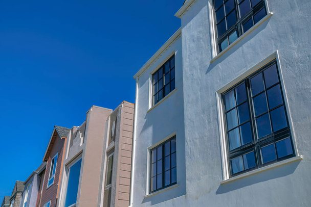 Дома с фотографией и стеклопакетами с видом на чистое небо в Сан-Франциско, Калифорния. Рядом со светло-коричневым домом с иллюминаторами справа стоит дом с остекленными окнами.. - Фото, изображение