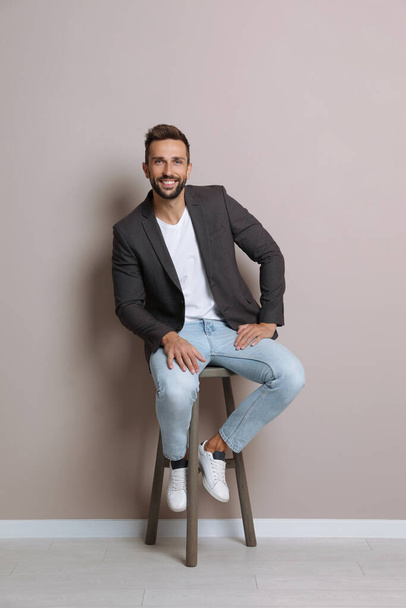 Handsome man sitting on stool near beige wall - Photo, image