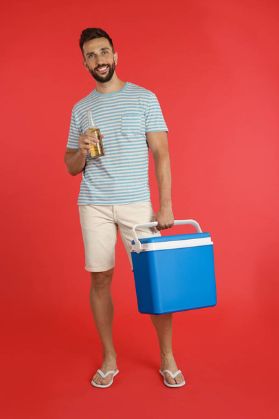 Happy man with cool box and bottle of beer on red background - Foto, imagen
