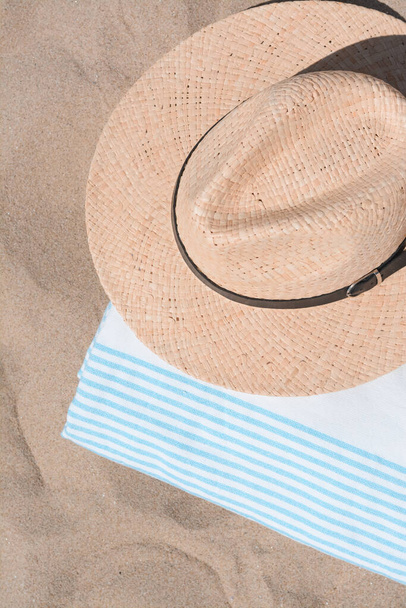 Straw hat and beach towel on sand, top view - Foto, Bild