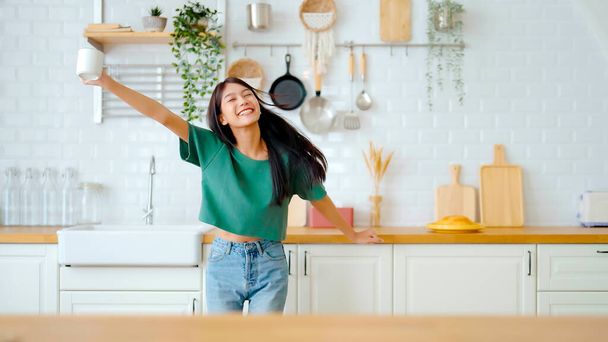 Asian young woman dancing in kitchen room. Female happy and relaxing at free time on weekend - Фото, изображение