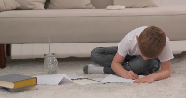 A fiú papíron rajzolja le a családját. A gyermek otthon rajzol és leül a padlóra. Egy fiú erőfeszítései által.. - Felvétel, videó