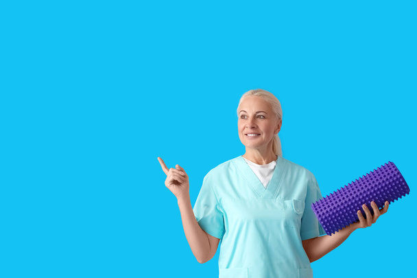Зрелый физиотерапевт с пенокатком, указывающим на что-то на синем фоне - Фото, изображение