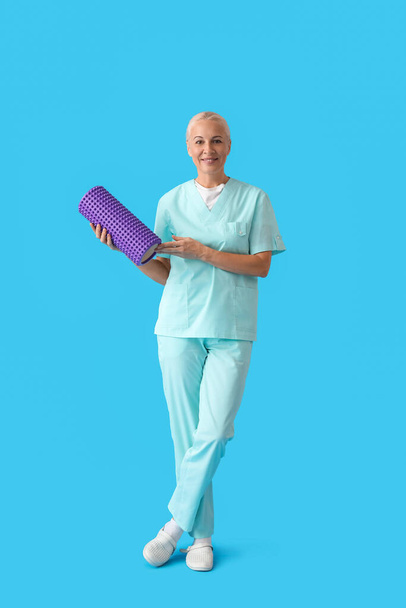 Mature physiotherapist with foam roller on blue background - Foto, afbeelding