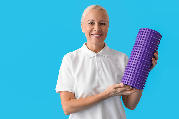 Mature physiotherapist with foam roller on blue background - Zdjęcie, obraz