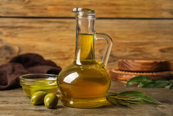 Decanter and bowl with fresh olive oil on wooden background - Fotoğraf, Görsel