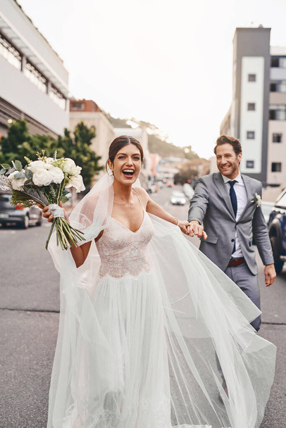 The bride is running away with her groom. a beautiful couple out in the city on their wedding day - Foto, Imagem