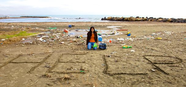Triste écologiste demandant de l'aide assis sur la plage pleine de saleté
 - Photo, image