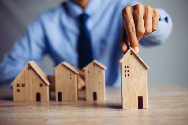 Geschäftsmann, der das Modell eines Mini-Holzhauses vom Modell auf dem Holztisch auswählt, plant, eine Immobilie zu kaufen. Konzept der Auswahl der besten. - Foto, Bild