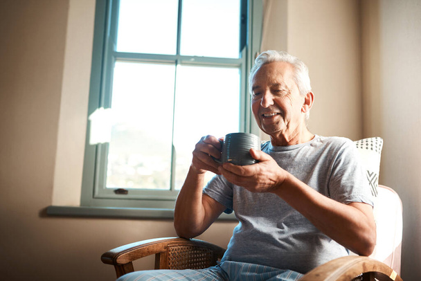 Нет ничего лучше, чем чашка кофе по утрам. счастливый пожилой человек, держащий чашку кофе и сидящий в кресле дома - Фото, изображение