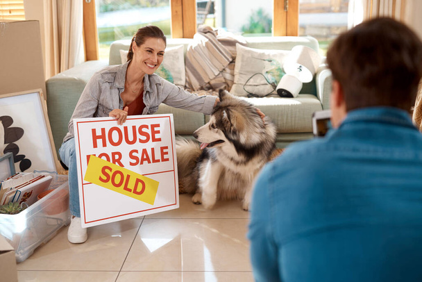 Were the proud owners now. a happy young couple and their dog taking photos with a sold sign in their new home - Foto, Imagem
