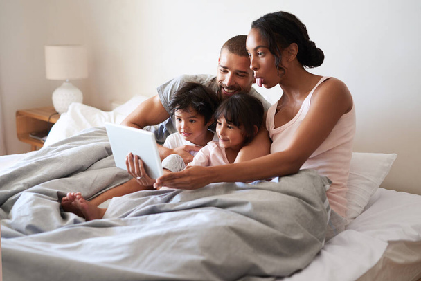 Were not camera shy over here. a beautiful young family of four taking selfies with a digital tablet in their bedroom - Foto, Imagem