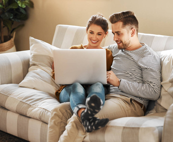 The internet has just what you need to keep busy. a young couple using a laptop while relaxing at home - Photo, Image