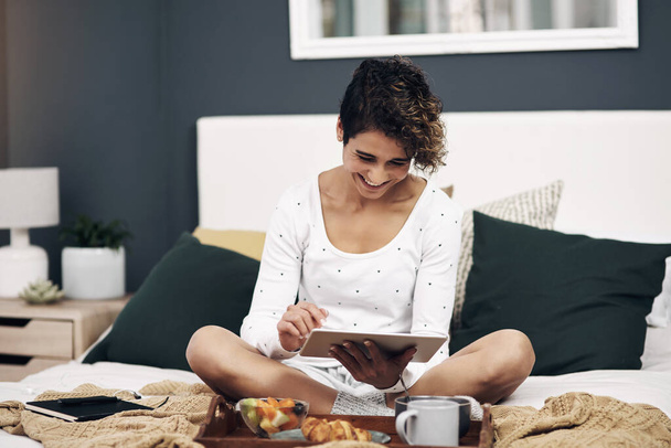Ελέγχω τα τοπικά στέκια. μια νεαρή γυναίκα που χρησιμοποιεί ένα ψηφιακό δισκίο, ενώ το πρωινό στο κρεβάτι στο σπίτι - Φωτογραφία, εικόνα