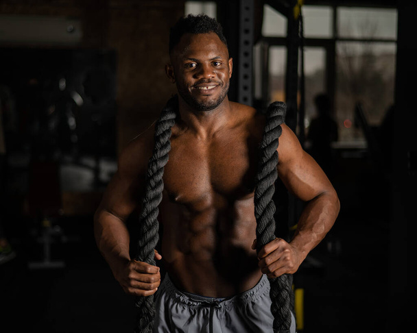 Muscular african american man posing with rope in gym - Foto, Bild