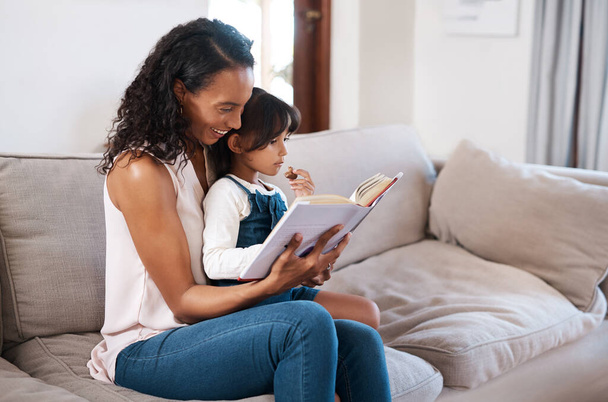 Bonding time involves reading our favorite books. a young girl reading a book while sitting with her mother at home - Foto, Imagen