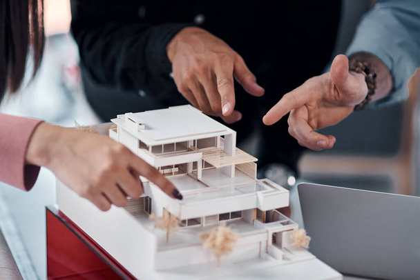 Мы все играем ключевую роль в этом проекте. Три неузнаваемых архитектора, работающие вместе над макетом современного дома в своем офисе - Фото, изображение