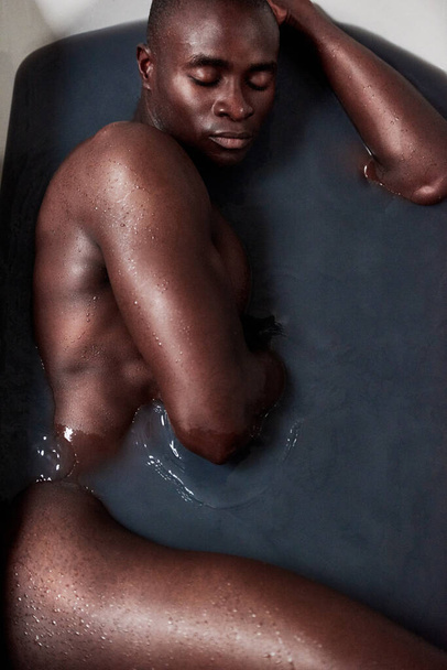 Real men take baths. a handsome young man submerged in a bath filled with dark water - Fotó, kép