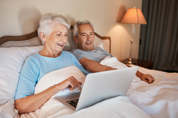 Technology makes it easier to share photographs. a happy senior woman using a laptop and sitting in bed with her husband at home - Foto, Imagem