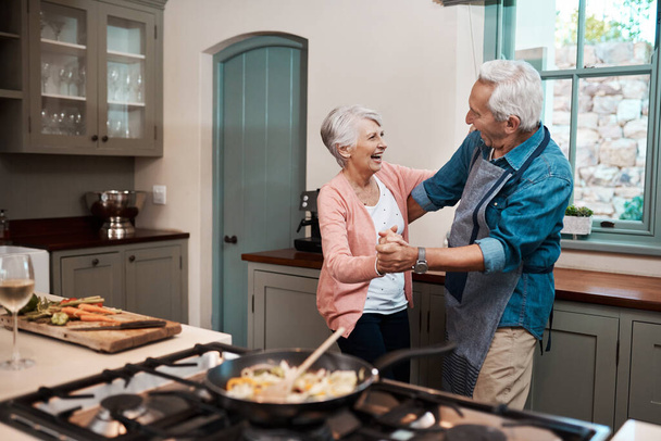We know how to keep our love going strong. a senior couple dancing while cooking in the kitchen at home - Photo, image