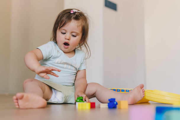 Cute baby girl playing with colorful blocks sitting on a floor at home. Baby development. Educational toys for young children. Construction block for baby or - Photo, Image