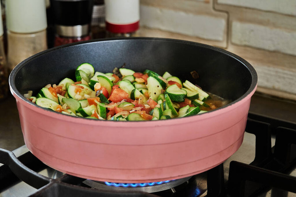 Zucchini sliced in half rings with tomatoes are fried in pan, on gas stove. - Foto, Bild