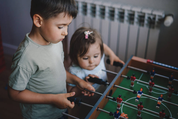 Big brother spending playtime with his younger sister playing foosball together. Sports football game. Happy family. - Foto, afbeelding