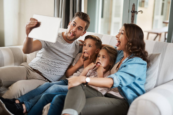 Silly selfies are the best selfies. a young family of four taking selfies together with a digital tablet on the sofa at home - Valokuva, kuva