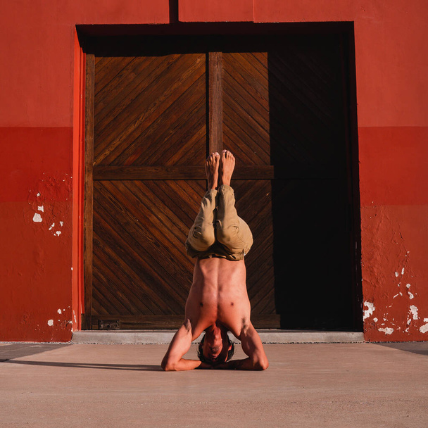 Latin athlete doing a handstand doing an extreme exercise. Hispanic man doing yoga. Muscular Hispanic guy raised up with his hands up with an old house in the background. Latino athlete carrying his body. - Valokuva, kuva