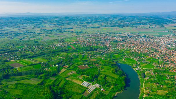 Above view on lake, forest, colorful hilly landscape with cottage settlement, several greenhouses on cultivated arable plots, farmland, city in the distance. - Photo, Image