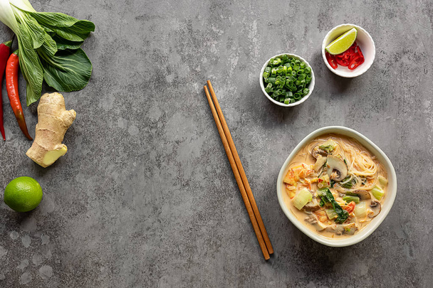 Bowl of curry laksa, a spicy glass noodle dish popular in Southeast Asia with prawns, bok choy, lime, ginger, and chili. Most variations of laksa are prepared with a rich and spicy coconut soup. - Foto, immagini