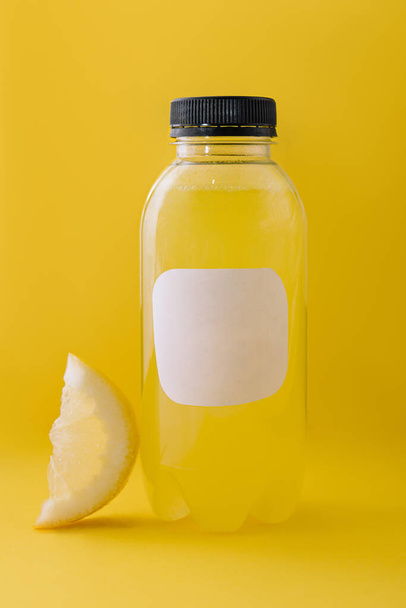 Bottle of fresh lemon juice on yellow background - Fotó, kép