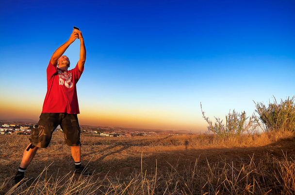 Ένας ενήλικας τραβάει φωτογραφίες με το κινητό του το ηλιοβασίλεμα. - Φωτογραφία, εικόνα