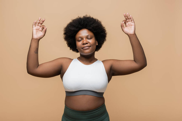 pleased and curly african american plus size woman in crop top gesturing isolated on beige - Foto, Imagen