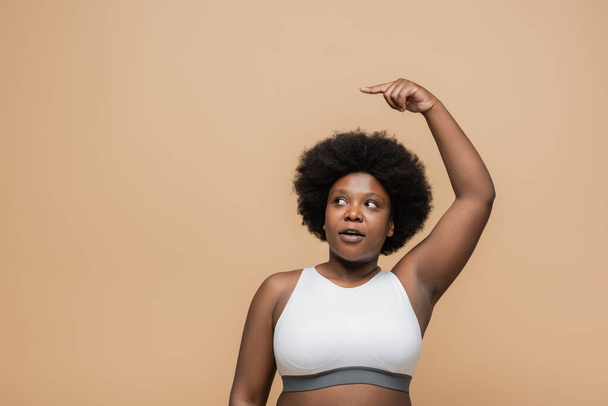 curly african american plus size woman with raised hand pointing with finger isolated on beige - Foto, Imagem