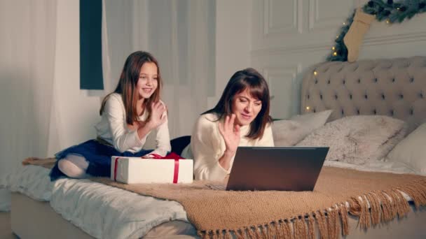 Mother and child communicate remotely with their father through laptop video communication. New Years Eve, festive evening. the girl shows a box with a gift. - Video