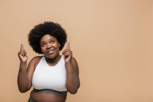 cheerful african american plus size woman in crop top pointing with fingers isolated on beige - Foto, Bild