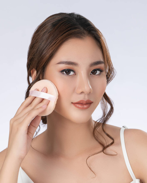 Face make up concept. Portrait of gorgeous young girl applying dry powder foundation. Beautiful model putting makeup powder with cosmetic cushion on her face. - Photo, Image