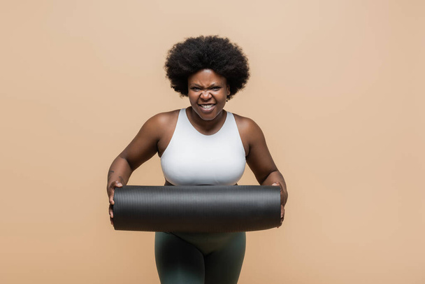 african american plus size woman in crop top grinning and holding fitness mat isolated on beige - Φωτογραφία, εικόνα