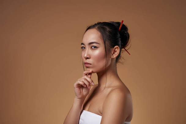 Cropped side view of thoughtful stylish asian girl. Attractive young brunette woman wearing tank top. Female beauty. Isolated on orange background. Studio shoot. Copy space - Foto, imagen